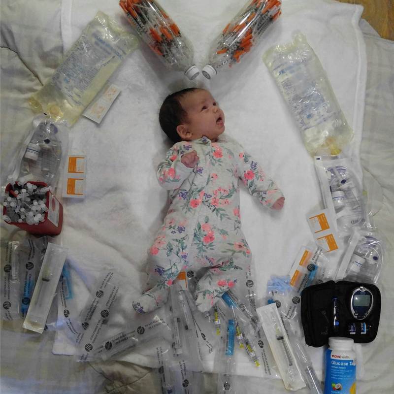 Image of a dark haired newborn girl surrounded by a heart made of supplies her mother used during pregnancy for both HG and gestational diabetes 